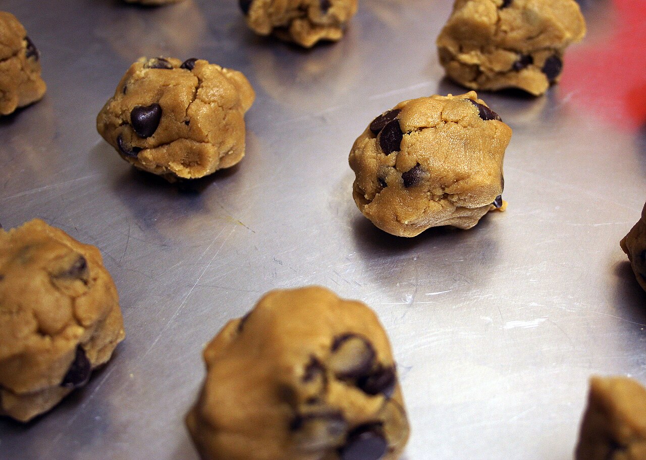 Balls of chocolate chip cookie dough spaced across a metal baking sheet.
