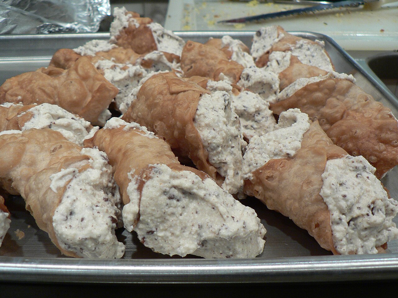 Cream-filled cannoli piled on a rectangular metal tray with raised edges.